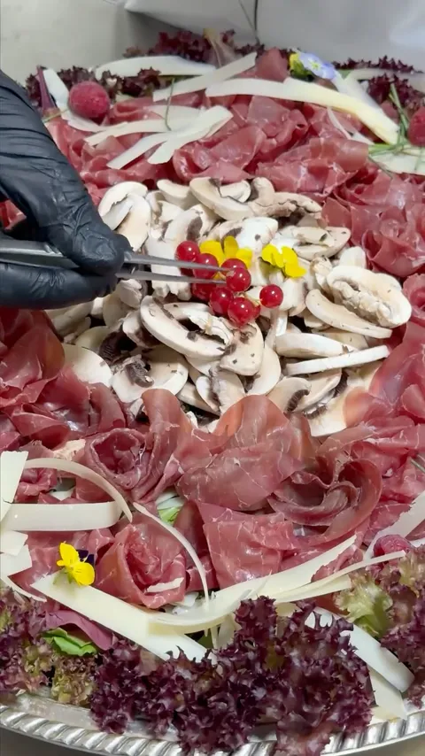 A chef plating a carpaccio and mushroom platter with tweezers.